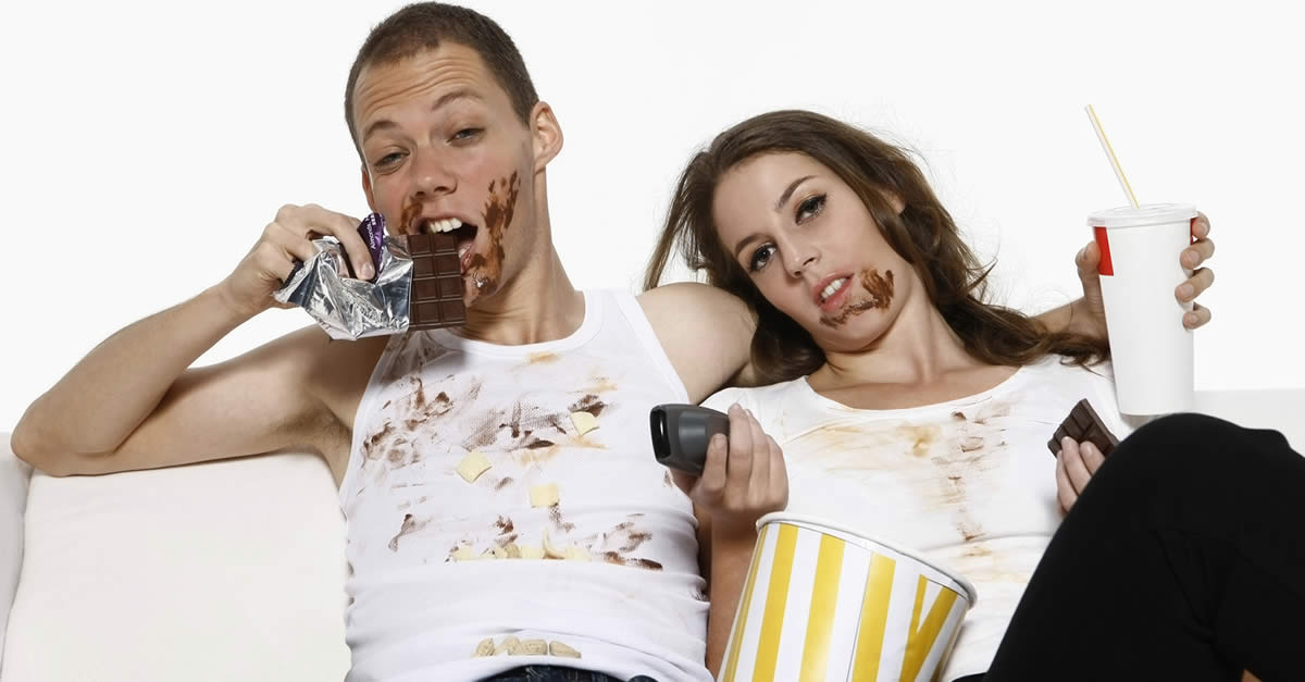 Man and woman eating while watching television on couch