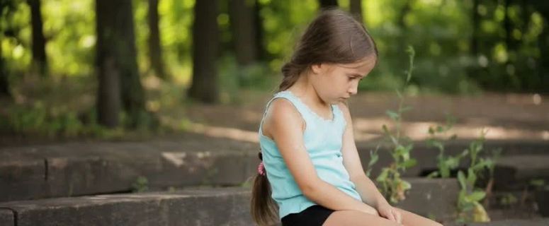Sad little girl sits alone in the park